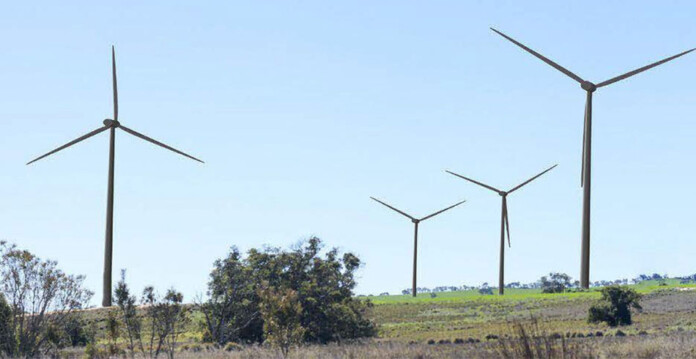 Four wind turbines among scrub in hillside with blue sky overhead