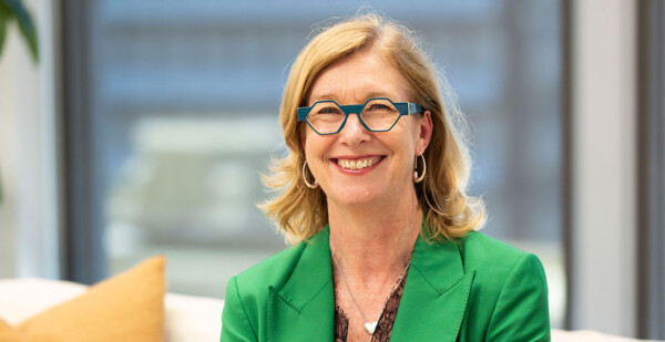 Close up of smiling woman wearing blue framed glasses and bright green jacket in office building