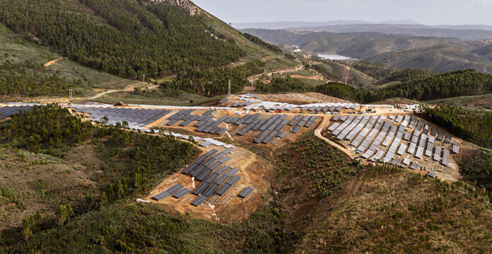Photo showing large solar farm set in hilly terrain with lush forest