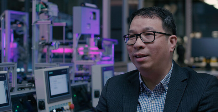Prof-alan-wong-rmit Man wearing glasses and a suit sits in computer lab illuminated by purple and blue lighting