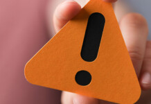 Planetwise Solutions banned from energy upgrades program Close up of hand holding orange warning sign with bold black exclamation point