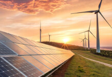 Renewables over 50%, wholesale prices down… Is the energy transition succeeding? Solar panels with wind turbines and beautiful orange sunset over coastline
