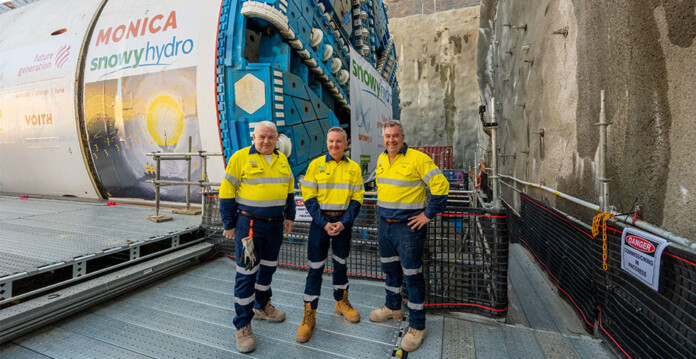snowy-hydro-tbm-monica Three men in high-vis workwear stand in front of massive tunnel boring machine