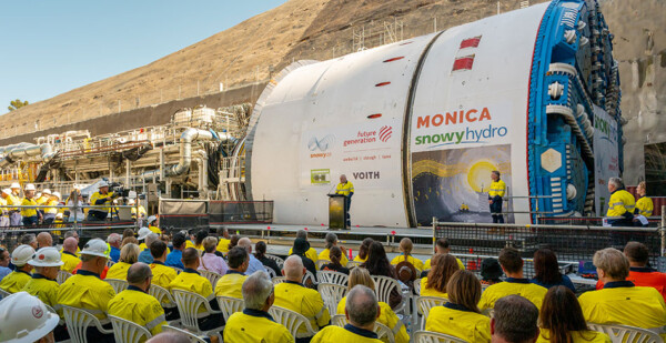 Tunnel boring machine on platform with speaker at lectern and crowd in foreground