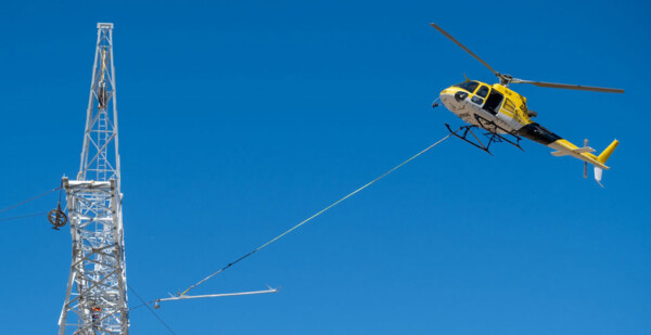 Helicopter strings transmission line with bright blue sky overhead