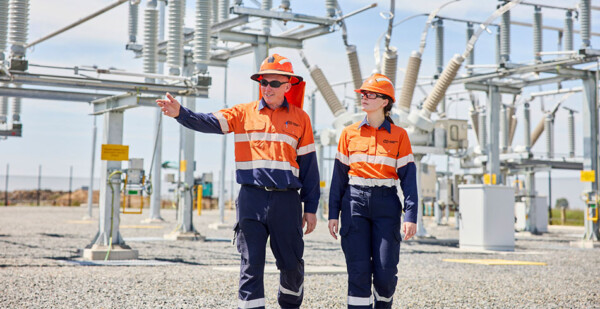 Two energy workers walk around observing substation infrastructure