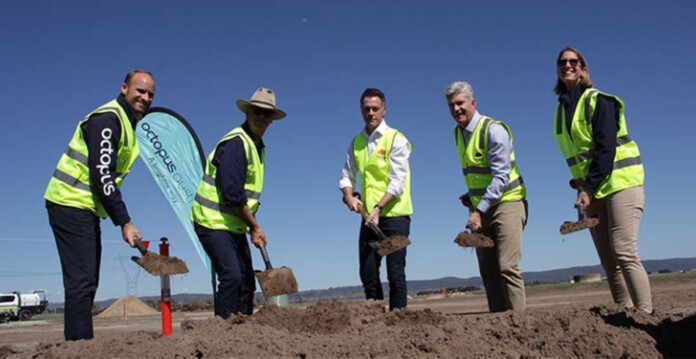 Five executives in high-vis vests use shovels to turn sods of dirt