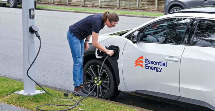 Woman charges white electric vehicle using an EV charger built into a streetlight