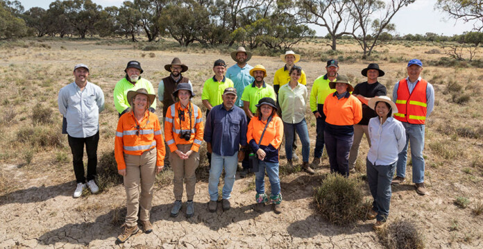 Group shot of people dressed in different forms of high-vis workwear at a grassy site with trees in the background