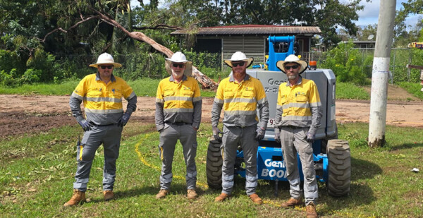 Power restoration crew of four men in high-vis workwear, with cyclone-affected vegetation in background