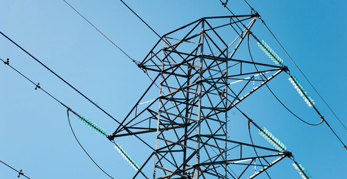 Close-up of a high-voltage transmission tower with blue sky overhead