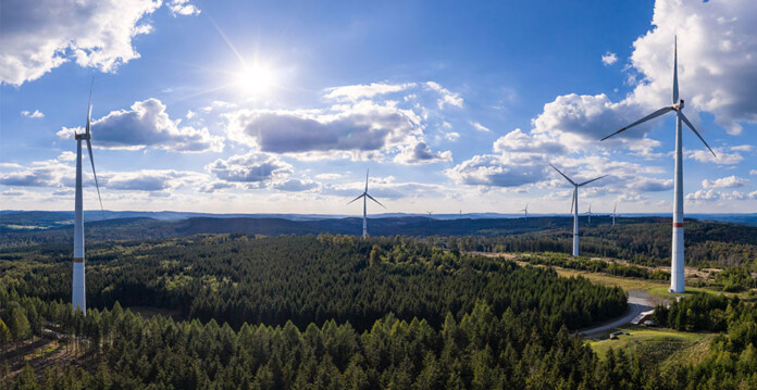 Wind turbines set in pine forest with blue cloudy sky overhead