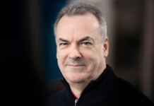 Powerlink Queensland announces appointment of new CEO Head and shoulders shot of smiling man wearing black shirt against mottled dark background