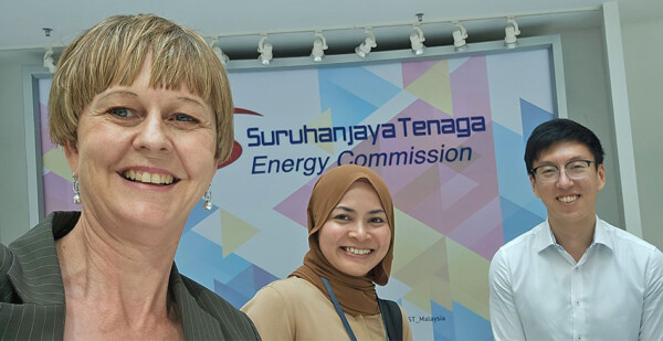 Three grid experts pose for photo in front of a banner 