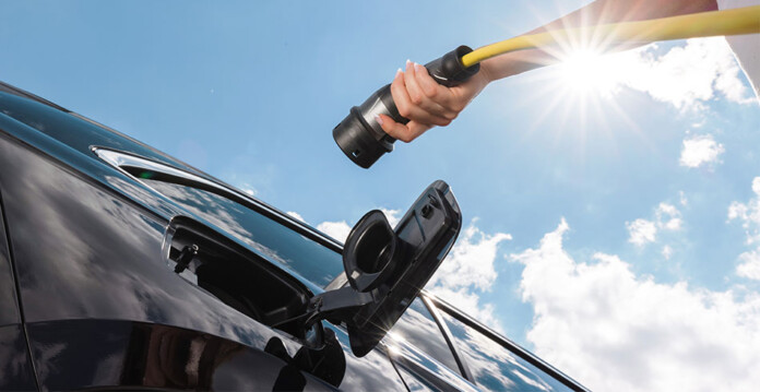 Upward view of female hand holding EV charger next to vehicle with blue sky and sun shining overhead