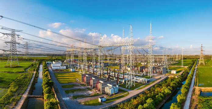 Image of transmission towers connecting to a substation with bright blue sky overhead