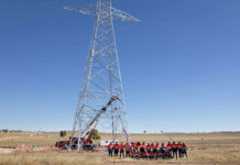 First transmission tower installed at Central-West Orana REZ Work crew gathers underneath first transmission tower erected at a renewable energy zone site with bright blue sky overhead