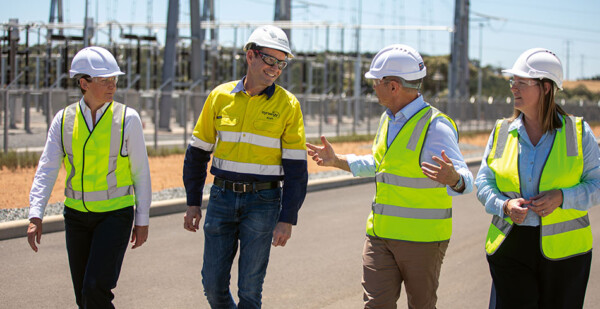 Four people in hard hats and high-vis vests walk and talk at site of big battery storage project