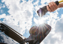 New research reveals Australia’s most EV-friendly cities Hand holding EV charger up to electric vehicle with blue sky and clouds overhead
