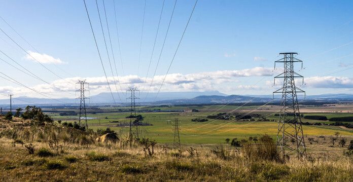Transmission towers in grassy rural area with blue sky overhead