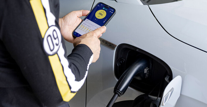 White electric vehicle charges while person holds smartphone with charging app on the screen