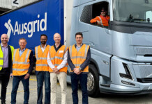 Optimised prime: Ausgrid trials heavy electric freight mover Five men in high-vis vests pose for photo in front of a heavy electric prime mover with an Ausgrid logo on the side