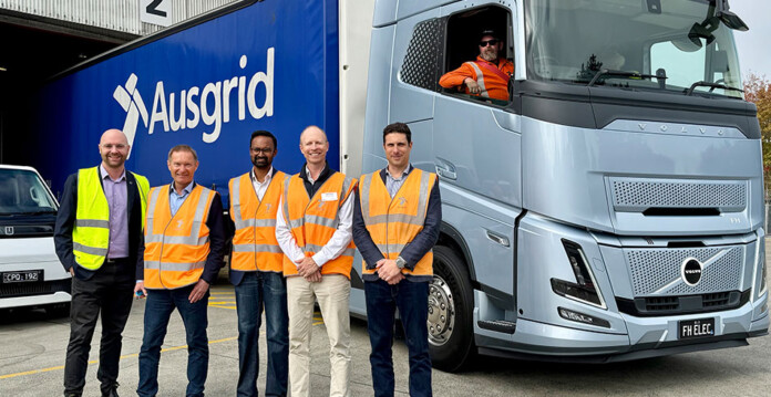 Five men in high-vis vests pose for photo in front of a heavy electric prime mover with an Ausgrid logo on the side