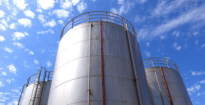 Three large concrete and steel fuel storage tanks with blue cloudy sky overhead
