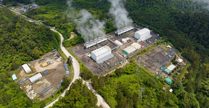 Steam pours from chimneys at a geothermal power station in a green mountainous region