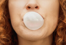 Renewables vs fossil fuels: Why can’t we walk and chew gum at the same time? Close up of woman with red curly hair blowing bubble with bubble gum