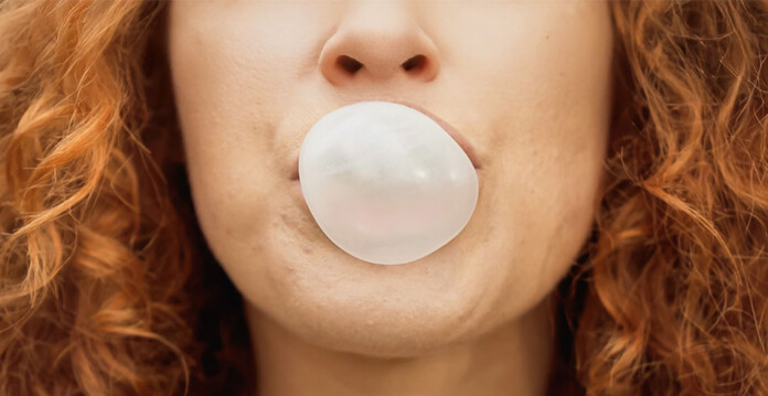 Close up of woman with red curly hair blowing bubble with bubble gum