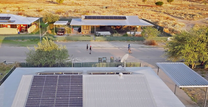 Aerial photo showing solar installation on rooftops in a remote community, with children playing soccer in the street
