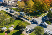 Giant equipment rolls across NSW for HumeLink build Aerial shot of a convoy transporting large pieces of transmission equipment along a road with trees and buildings on either side