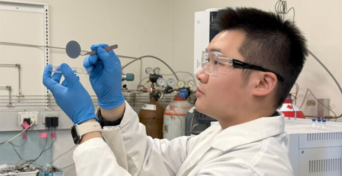 Researcher wearing white coat and blue gloves handles small membrane in laboratory