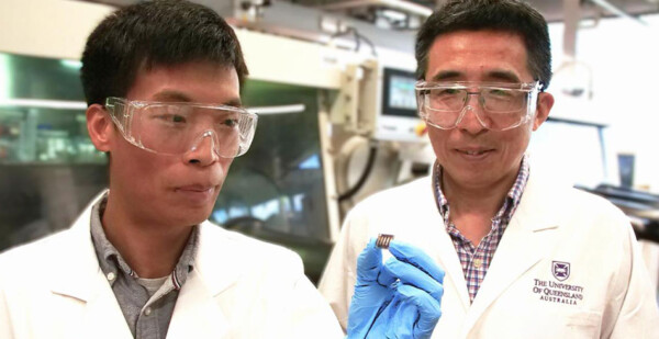 Two male researchers in white lab coats pose for photo with one holding a tiny solar cell 