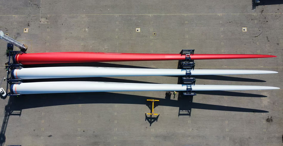 Vestas trials red turbine blades to mitigate bird collisions Aerial shot of three turbine blades positioned on the ground with one being bright red and the other two being a whitish grey