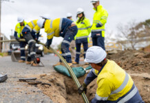 AusNet invests $8.2 million in gas network upgrade AusNet crew in hard hats and high-vis safety gear work in underground trench on roadside