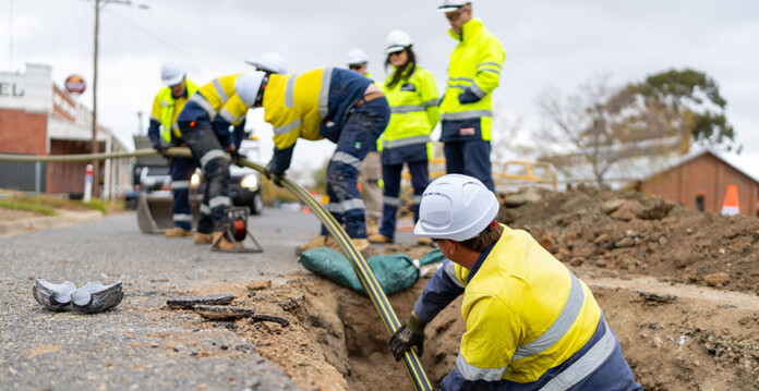 AusNet crew in hard hats and high-vis safety gear work in underground trench on roadside