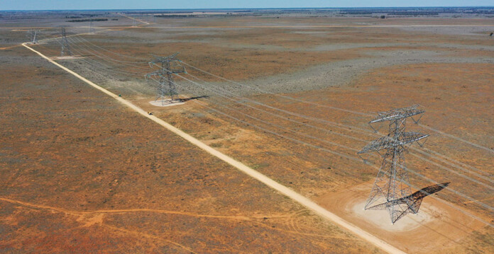 Transmission towers along dirt road in rural area with reddish dirt
