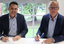 Enerven signs new five-year partnership with ElectraNet Two male executives sign agreement papers at a desk in a sunlit room