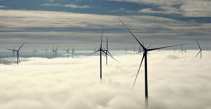 dozens of wind turbines above cloud line with blue sky overhead