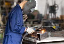 Aussie businesses the “missing middle” in solar and storage Male worker wearing a blue jumpsuit and face shield welding metal in industrial factory