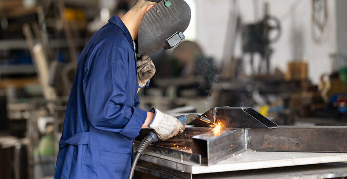 industrial-business Male worker wearing a blue jumpsuit and face shield welding metal in industrial factory
