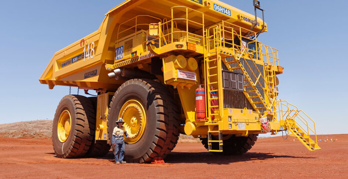 Worker stands beside massive yellow haul truck at a mining site in the Pilbara