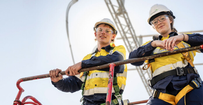 male and female energy workers atop structure wearing hard hats and safety gear