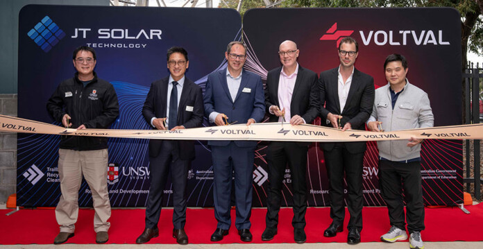 A group of researchers cut a ribbon in front of a wall bearing corporate logos