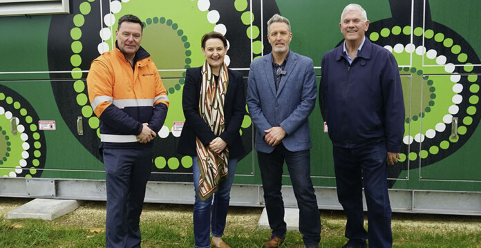 Four people stand in front of wall with Aboriginal art design for photo