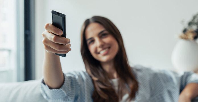 woman-using-power Smiling woman with long brown hair sits on couch in living room and uses a remote control