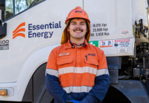 Essential Energy worker wins apprentice of the year award Smiling young man in safety workwear stands in front of Essential Energy-branded work vehicle