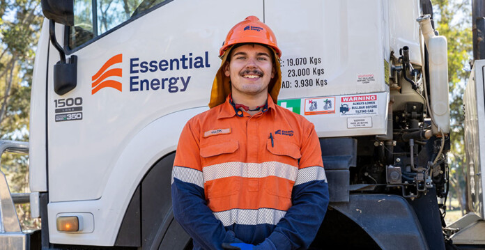Smiling young man in safety workwear stands in front of Essential Energy-branded work vehicle